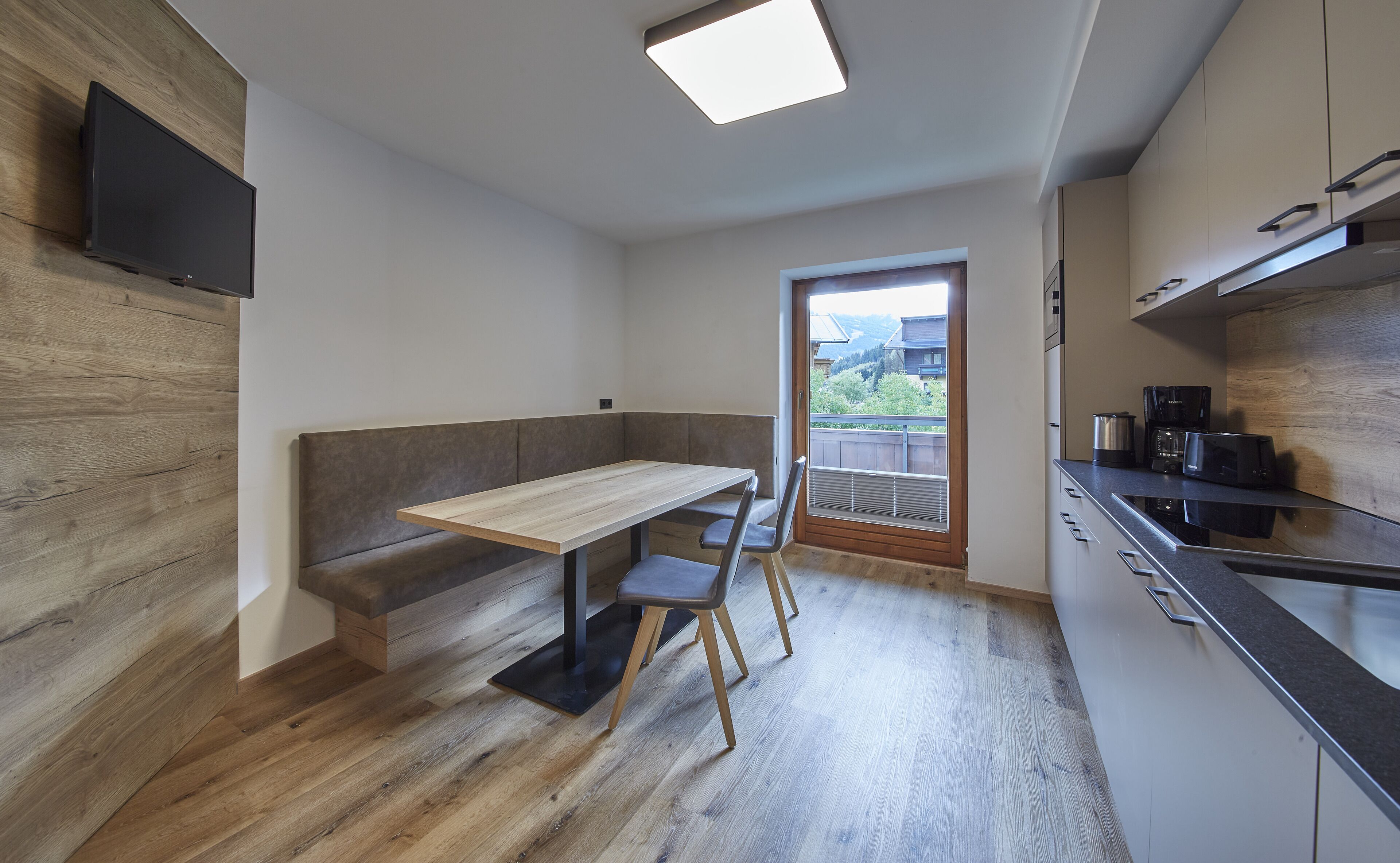 Une cuisine moderne avec un banc en bois, une table à manger et une vue sur l’extérieur.