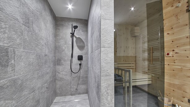 A modern bathroom with grey tiles, a glass shower enclosure, and wooden paneling. - Appartements Gappmaier (Saalbach-Hinterglemm)