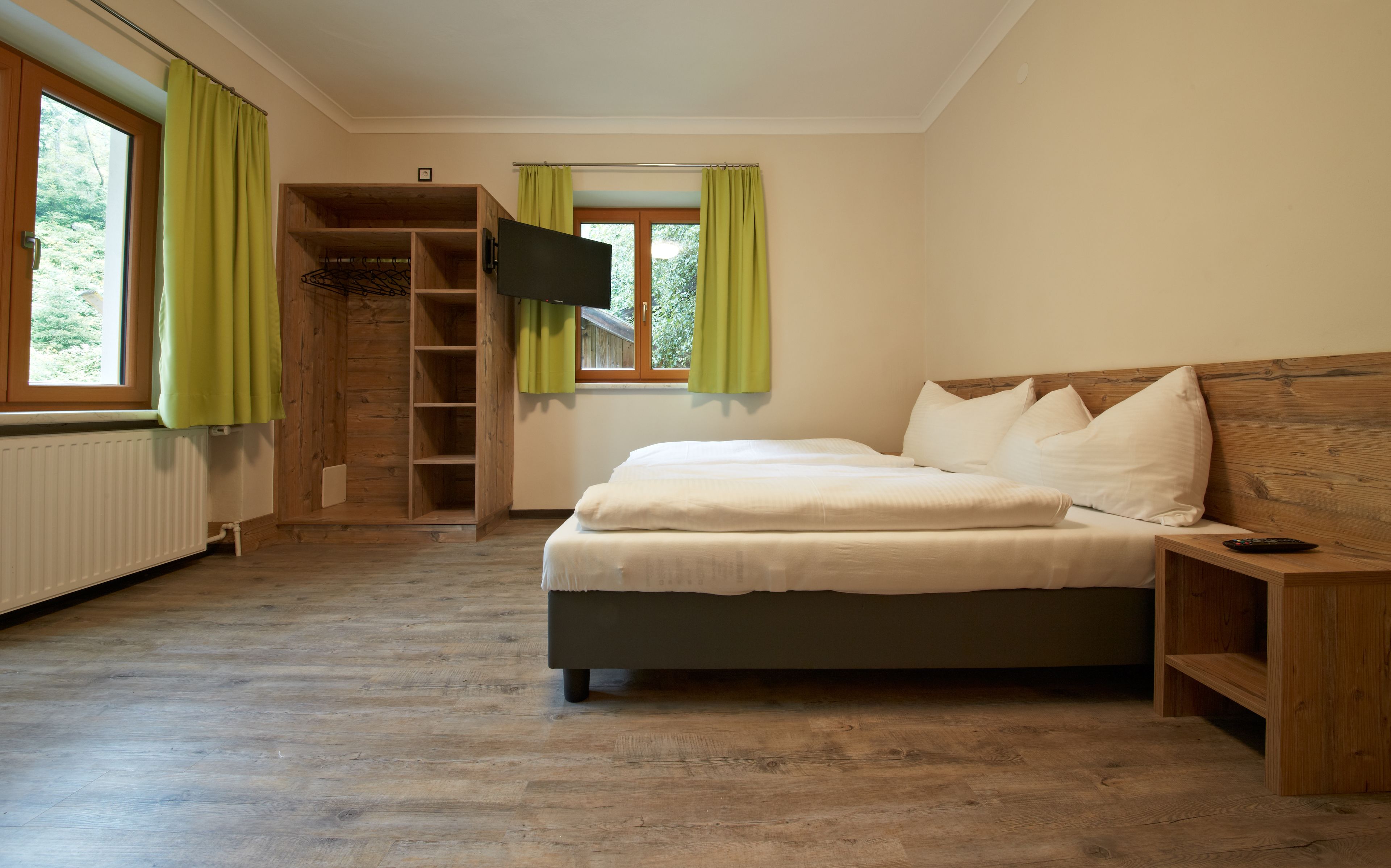 A bedroom with a bed, a TV, a wooden wardrobe, and a window with curtains.