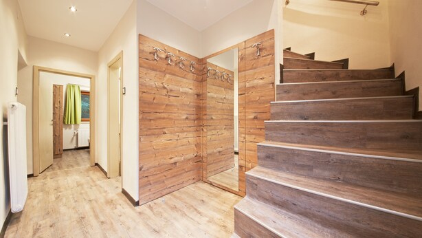 A wooden staircase leading to a second floor, a hallway with wooden flooring, and a mirrored closet door. - Holiday Lodge Central (Saalbach-Hinterglemm)
