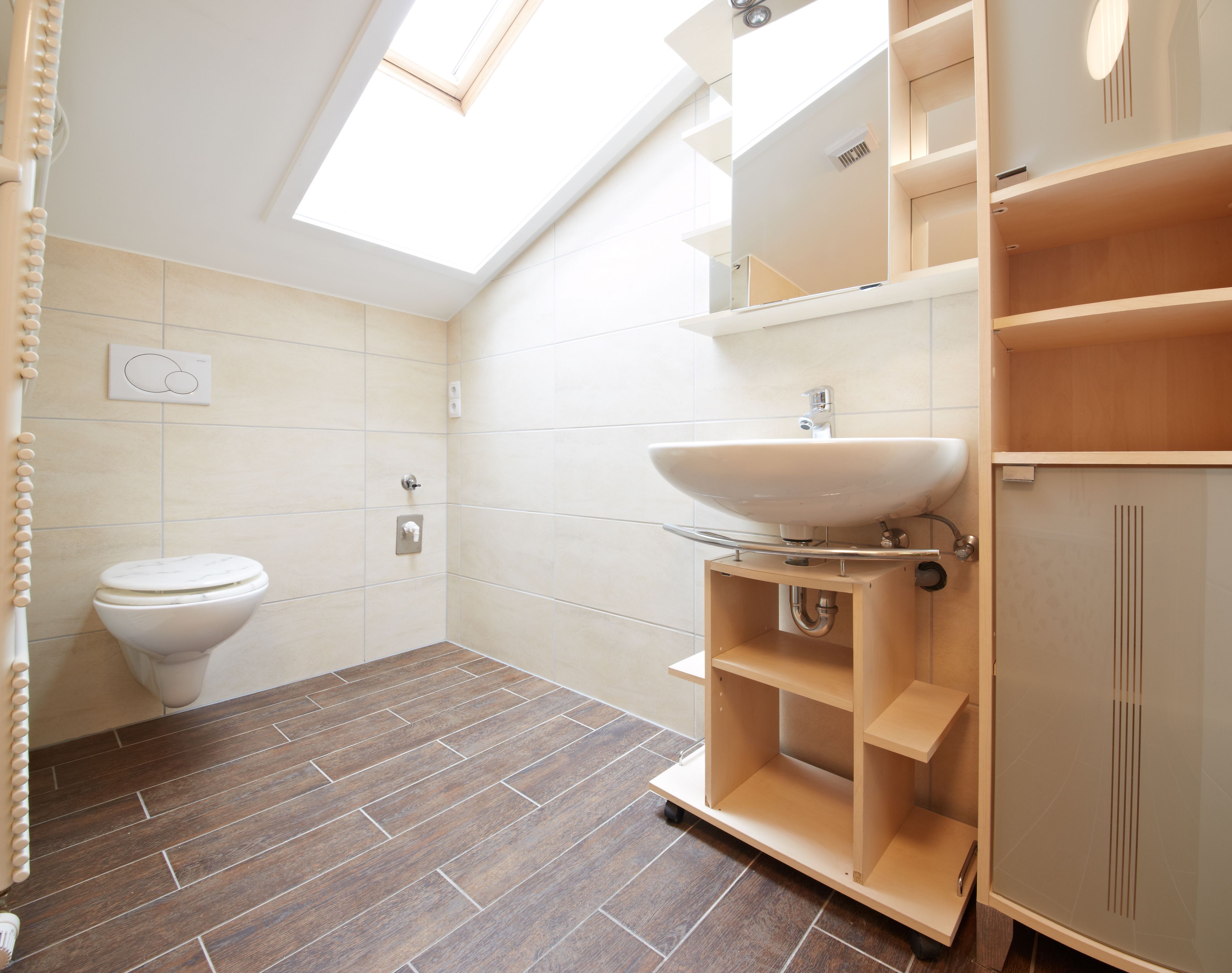 Un bagno moderno con finestra a lucernario, un water, un lavandino e scaffali in legno.