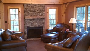 A cozy living room with a stone fireplace, leather sofas, and large windows. - Get Away From It All - Romantic or Family - Timberframe Cottage (Rome)