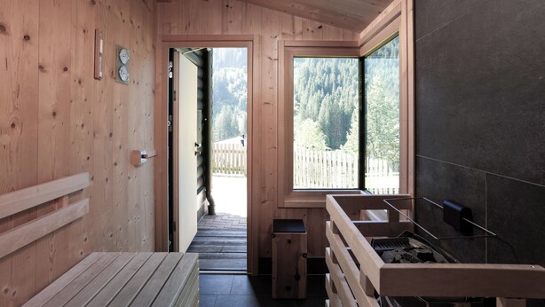 A wooden interior with a sauna, a view of a forest, and a stone wall. - FIVE SEASONS | Hideaway Saalbach (Saalbach-Hinterglemm)