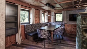 A cozy cabin interior with a wooden ceiling, a dining table with patterned chairs, a bench, and a TV mounted on the wall. - FIVE SEASONS | Hideaway Saalbach (Saalbach-Hinterglemm)