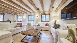 Un salón espacioso con sofás blancos, una mesa de centro de madera y vigas de madera a la vista en el techo.