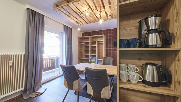 A modern kitchen with wooden cabinets, a dining table with chairs, and a coffee maker on the counter. - Time for Sport Appartements (Saalbach-Hinterglemm)