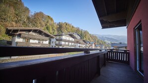 A wooden balcony with a view of traditional buildings and a forested hillside. - Time for Sport Appartements (Saalbach-Hinterglemm)
