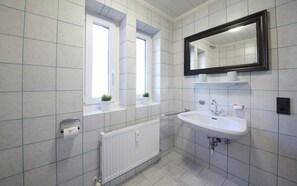 A modern bathroom with a white sink, a mirror, and two windows.