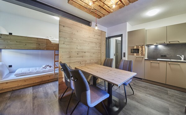 A compact living space with a bunk bed, a dining table with chairs, a kitchenette, and a wooden accent wall.