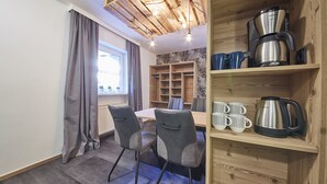 A modern dining area with a wooden table and chairs, a coffee machine, and a shelf with mugs and a kettle. - Time for Sport Appartements (Saalbach-Hinterglemm)