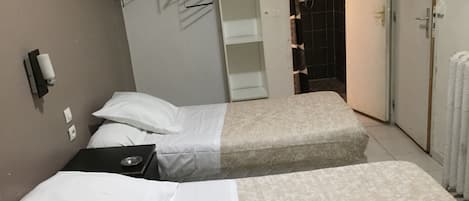 A hotel room with two beds, a wardrobe, a bathroom with a shower, and a towel rack.