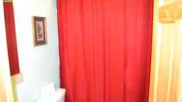 Un baño con cortina de ducha roja, inodoro blanco y un cuadro en la pared.