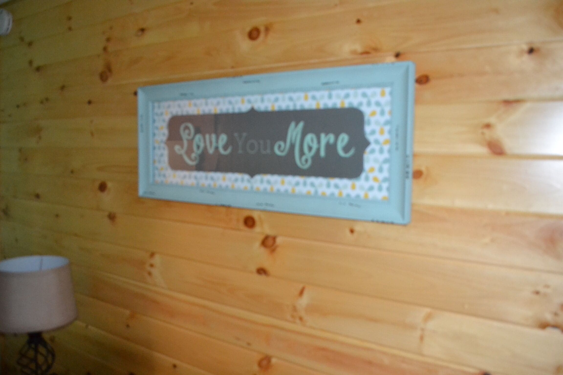 A framed sign with the text 'Love You More' on a wooden wall.