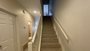 Un escalier avec une rampe, des murs blancs et une porte sur le côté gauche.