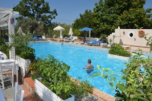 Ein Swimmingpool mit Liegestühlen und Sonnenschirmen, umgeben von viel Grün und einem weißen Gebäude.