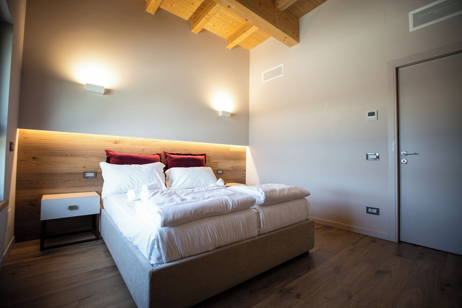 Une chambre à coucher avec une tête de lit en bois, un lit avec une literie blanche, une table de chevet et une porte avec une serrure.