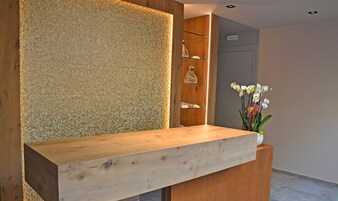 A reception desk with a wooden finish, a textured wall, and a vase with white flowers.
