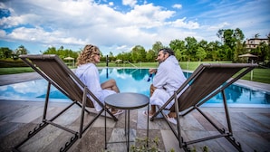 Two people in white bathrobes sitting on lounge chairs by a pool with a clear sky. - Cobue Wine Resort & SPA (Pozzolengo)