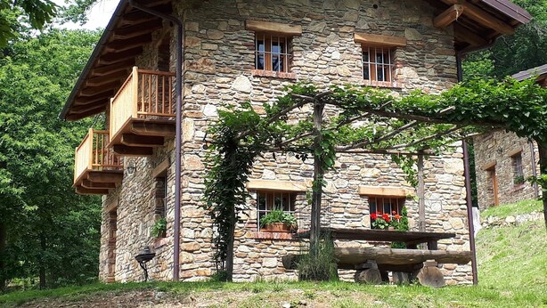 Une maison en pierre avec un balcon en bois et une pergola couverte de vignes.