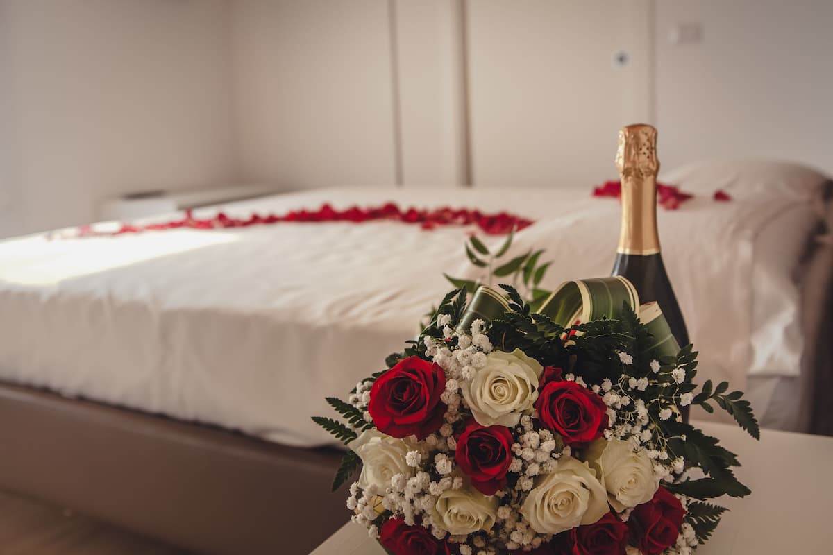 A bed with white bedding and a red rose petal arrangement.