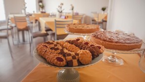 A dining area with a table set for a meal, featuring a variety of pastries and a cake on a glass stand. - Terra Ferma Rooms & More (Salzano)