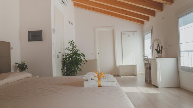 A modern bedroom with a large bed, a desk, a chair, a potted plant, and a window. - Terra Ferma Rooms & More (Salzano)
