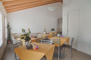 A dining area with multiple tables and chairs, potted plants, and a white door. - Terra Ferma Rooms & More (Salzano)
