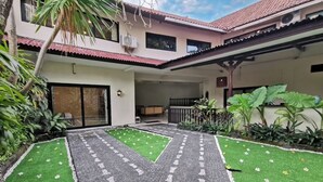 Un patio con un camino empedrado, césped artificial verde y diversas plantas.