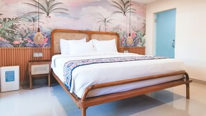 Una cama bien hecha con sábanas blancas y una manta de estampado floral, un cabecero de madera y un mural en la pared con follaje tropical.