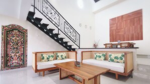 Una sala de estar moderna con un banco de madera, dos sofás con cojines verdes, una mesa de centro de madera, una escalera con barandillas negras y una puerta decorativa.