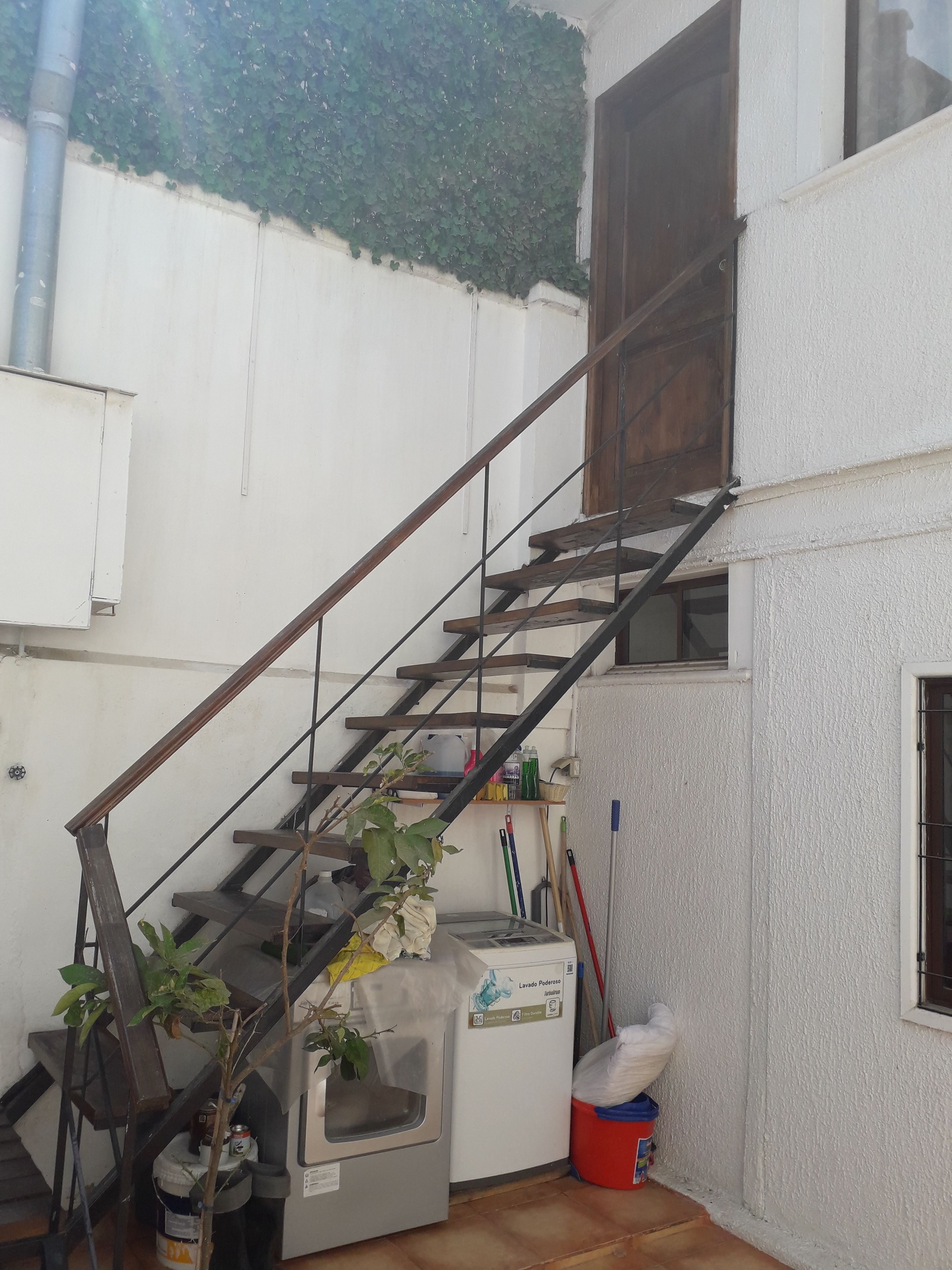 A staircase with a metal railing leading to a second floor. A washing machine is placed against the wall, and cleaning supplies are visible.