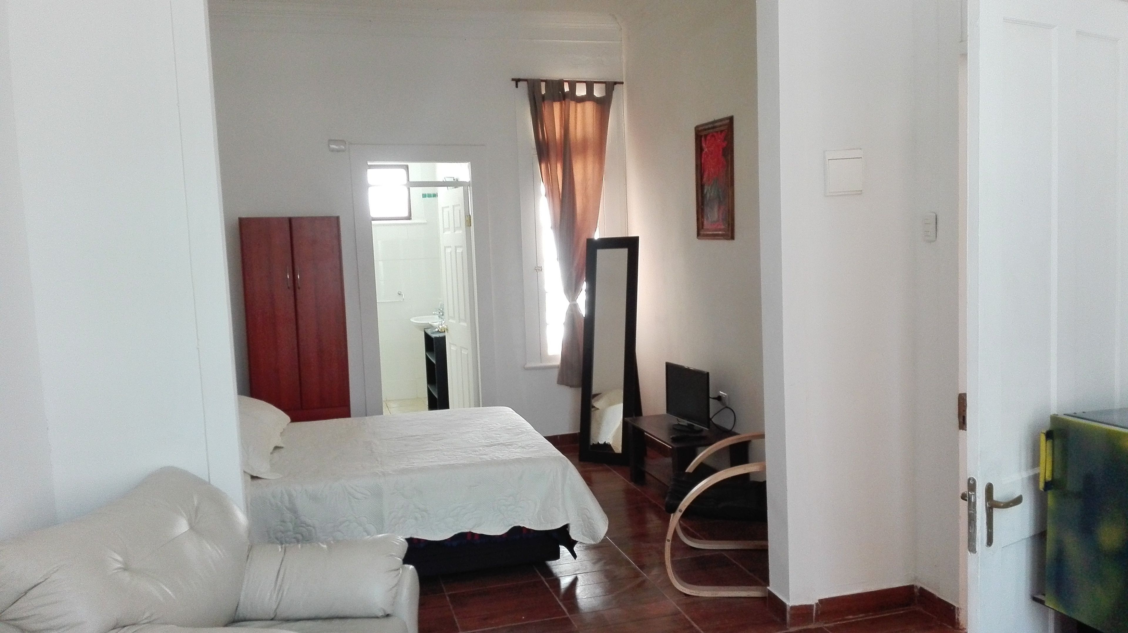 A bedroom with a bed, a wardrobe, a desk with a computer, and a mirror.