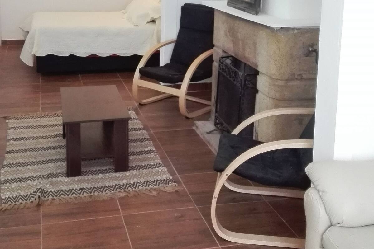 Una habitación con una cama, dos sillones, una mesita y una chimenea.