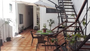 Een terras met een tafel en stoelen, omringd door potplanten, en een metalen trap.