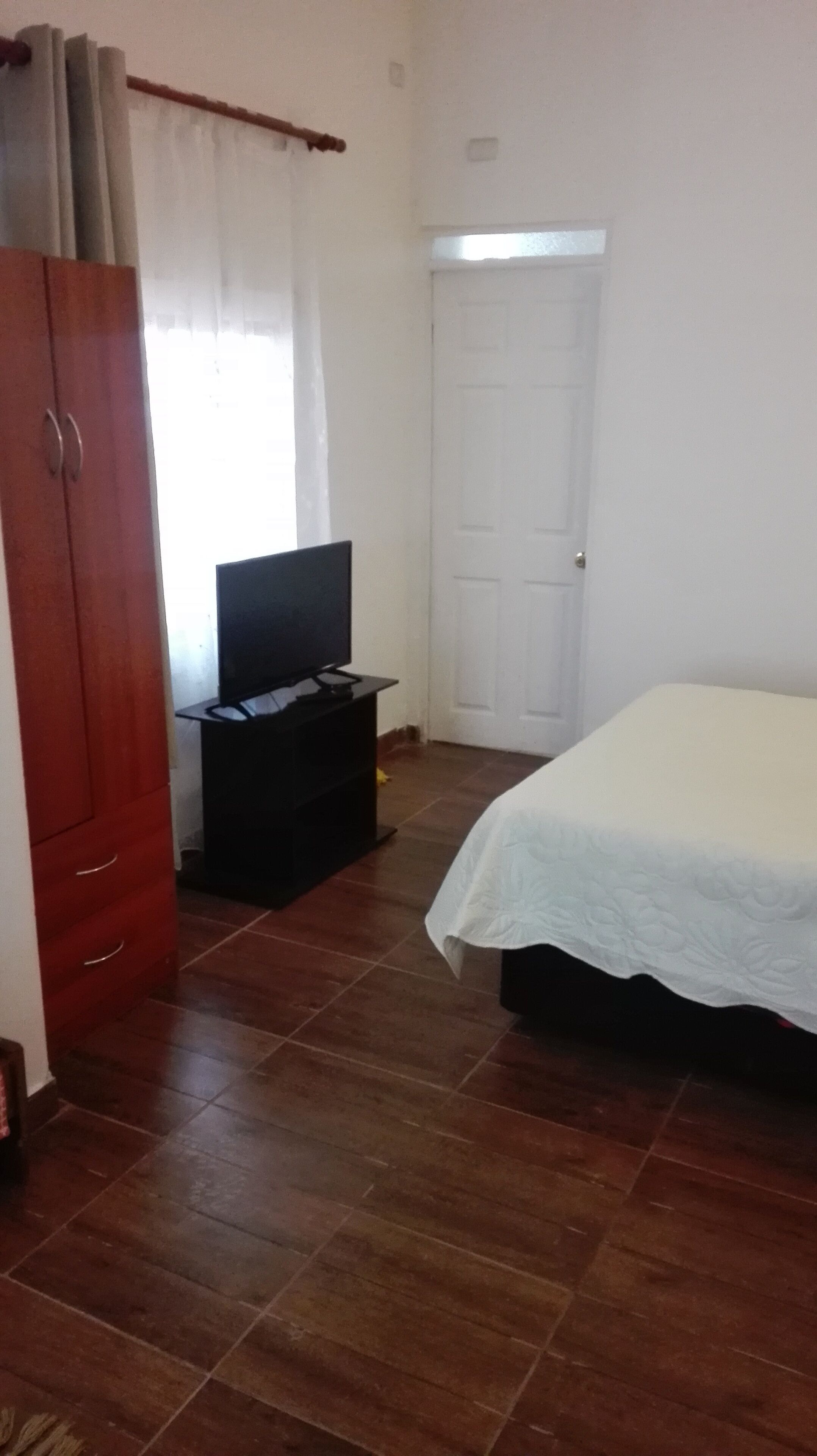 Un dormitorio con cama, televisión sobre un mueble, armario y puerta.