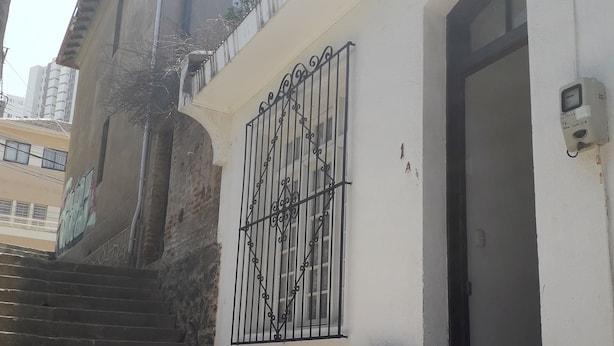 Een gebouw met een witte gevel, een metalen poort en een deur met een beveiligingscamera.