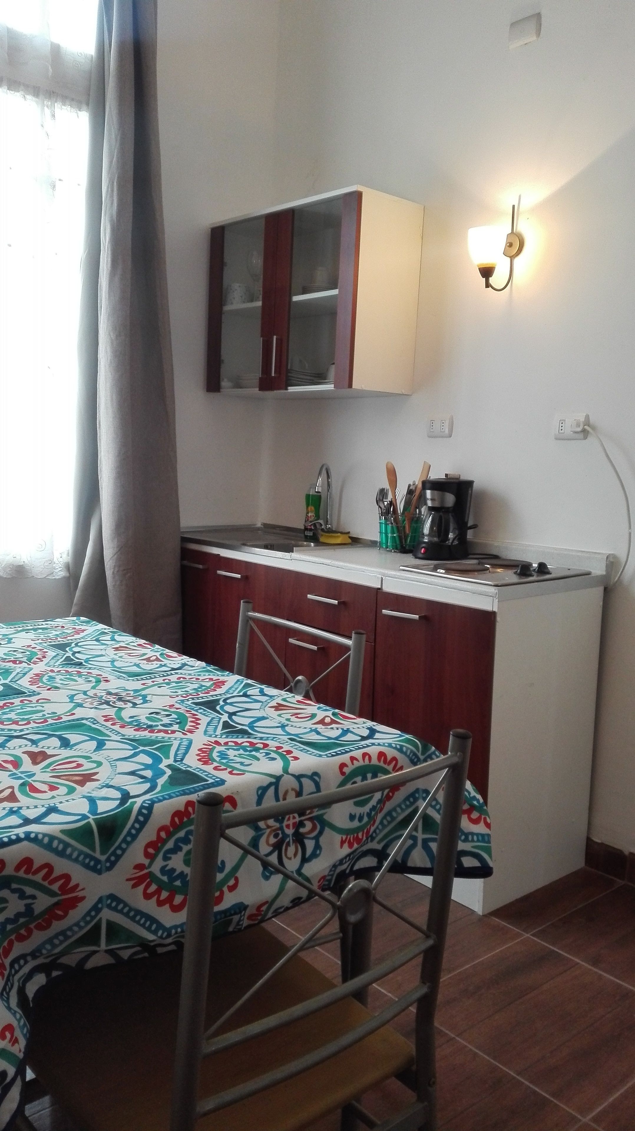 A compact kitchen with a dining area, featuring a table with a patterned tablecloth, a coffee maker, and a cabinet above the counter.