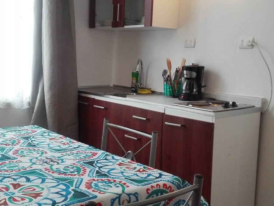 A compact kitchen with a dining area, featuring a table with a patterned tablecloth, a coffee maker, and a cabinet above the counter.