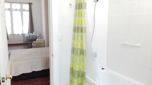 Een badkamer met douchegordijn, badkuip en een witte betegelde muur.