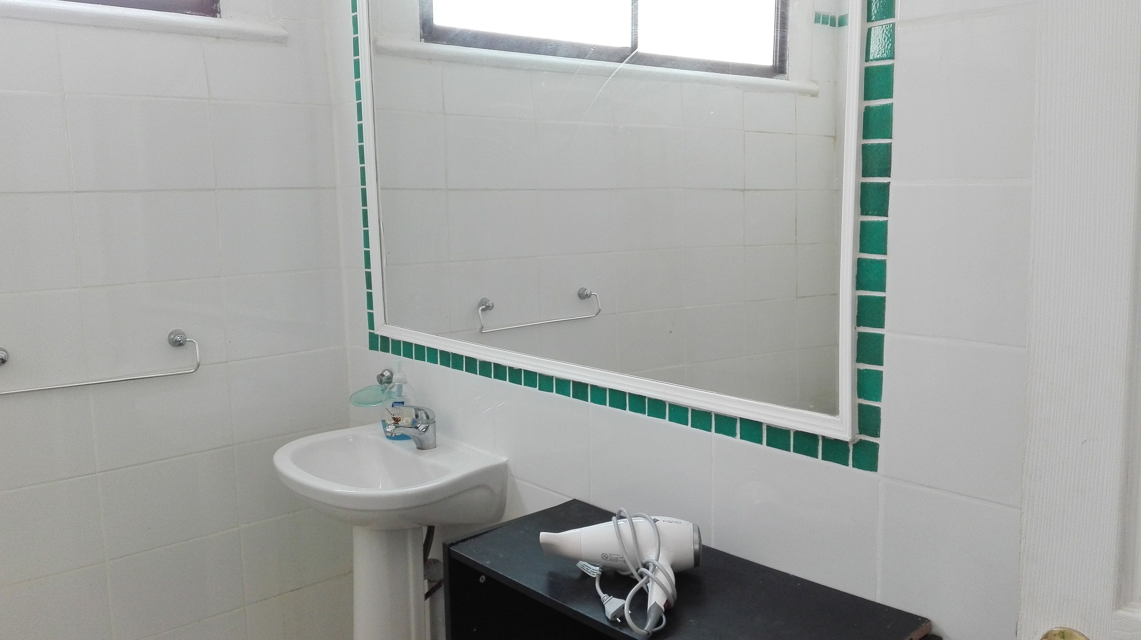 Un baño con un lavamanos blanco, un espejo y una ventana.