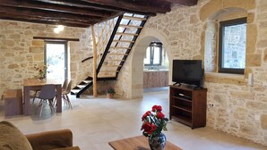 A rustic interior with stone walls, a wooden staircase, a dining area, and a TV stand. - Traditional Villa in Fres (Apokoronas)