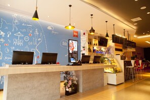 Un espace d’accueil moderne, avec un mur bleu orné de dessins fantaisistes sur le thème du voyage et un écran numérique affichant l’heure.