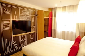 Une chambre d’hôtel avec un lit, un téléviseur fixé au mur, une armoire et une fenêtre avec des rideaux.