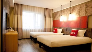 Habitación de hotel con dos camas, un escritorio de madera y un ventanal con cortinas.