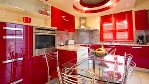 Une cuisine moderne avec des meubles de rangement rouges, des appareils électroménagers en acier inoxydable et une table à manger en verre.