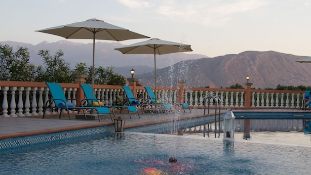 Un espace piscine agrémenté de chaises longues et de parasols, entouré d’une balustrade et avec des montagnes en toile de fond.