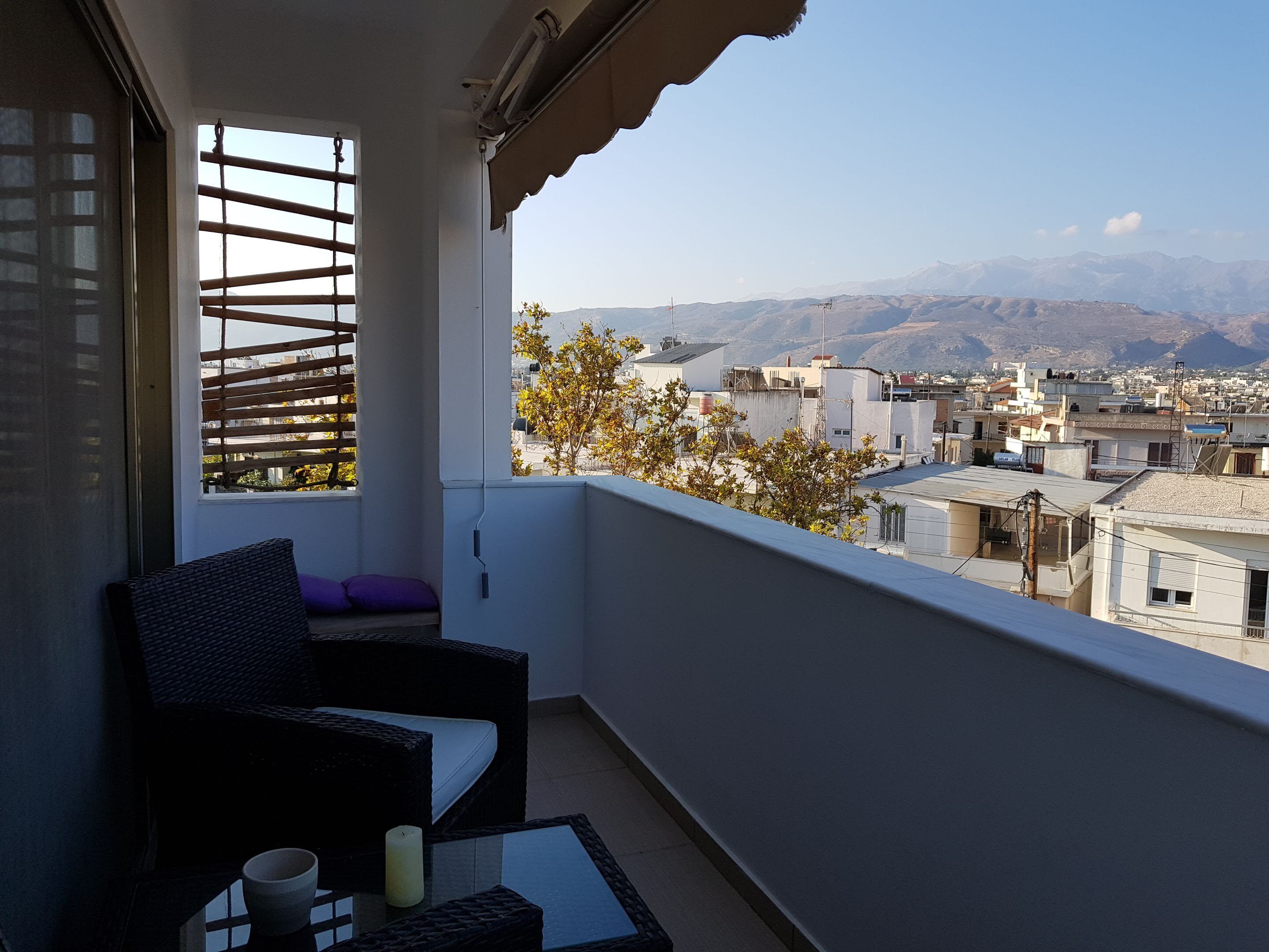 A balcony with wicker furniture, a view of a cityscape and mountains in the distance.