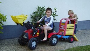 Deux enfants sont assis sur des petits tracteurs jouets devant un bâtiment.