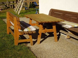 A wooden bench and table set outdoors with a grassy area and a wooden fence in the background.