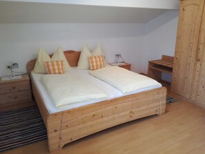 Una cama de madera con colchón blanco y almohadas a rayas, una mesita de noche con lámpara y un armario de madera.